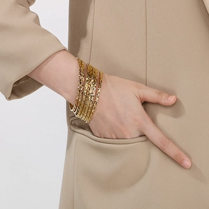 Close-up of stacked gold diamond-patterned bangles worn by model on a grey backdrop