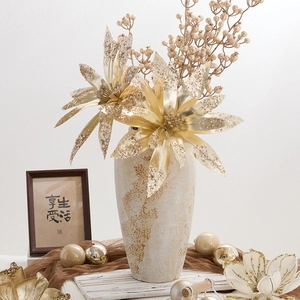Golden artificial Christmas flowers in ivory ceramic vase with festive home decorations