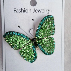 Macro detail of butterfly brooch with emerald and mint green crystals on a white base