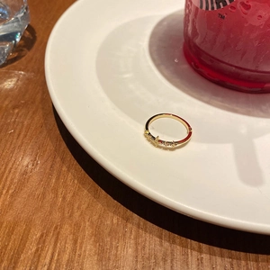 Detailed view of a gold-plated bow ring with small star zircons on a white ceramic plate
