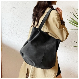 Detail of a large black matte tote bag worn on shoulder with a classic trench coat