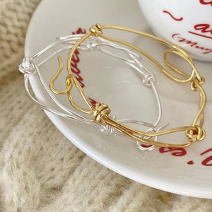 Macro detail of handmade knotted wire bracelets in gold and silver on white ceramic plate
