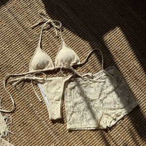 Detailed view of beige floral lace 3-piece bikini set and cover-up on a straw mat