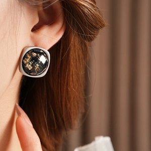 Gros plan de boucles d'oreilles carrées en résine noire avec paillettes dorées et bord argenté