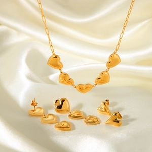 Dettaglio di un set di gioielli a cuore dorato con collana e orecchini su seta bianca