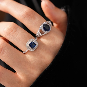 Detailed view of silver rings featuring square and oval blue stones on a model hand
