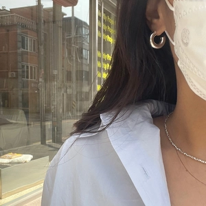 Close-up of minimalist silver hoop earrings and shiny beaded necklace on a model