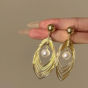Close-up of golden hollowed teardrop earrings with a white pearl held by fingers