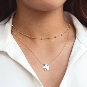 Collana a due strati con perline dorate e ciondolo a quadrifoglio bianco su una modella