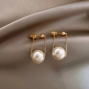 Detail of elegant C-shaped pearl drop earrings on champagne silk fabric background
