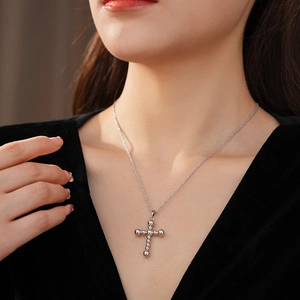 Gros plan d'un collier pendentif croix à perles argentées porté sur un vêtement noir