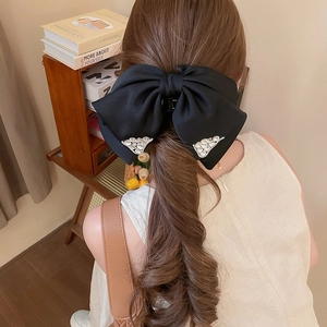 Detail of a large black satin bow hair claw with sparkling rhinestones worn on hair