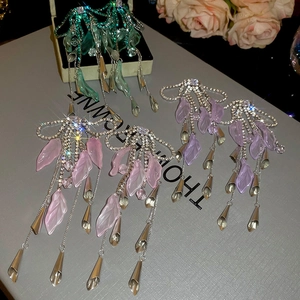 Macro detail of long tassel bow earrings with sparkling crystals and resin petals on a gift box
