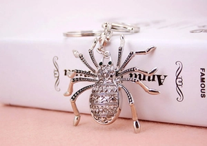 Macro shot of silver metal spider keychain featuring hollowed relief and green bead eyes