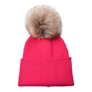 Detailed knit texture and fluffy raccoon fur pom-pom on bright pink kids winter beanie