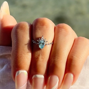 Close-up of a link chain ring with a blue pear-cut gemstone worn in bright outdoor light
