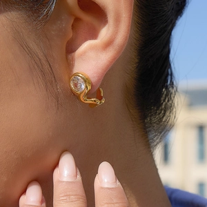 Golden streamlined earrings with round cubic zirconia on model under natural sunlight