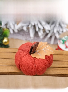 Macro shot of orange knitted pumpkin ornament with ribbed texture and felt leaf detail