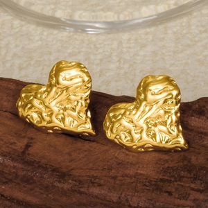 Detailed close-up of golden heart earrings with hammer texture on a wooden base