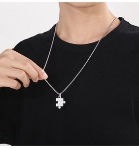 Detail of silver puzzle piece pendant necklace with puzzle engraving on box chain