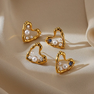 Detail of hollow heart earrings with pearls and blue zircon on beige satin fabric