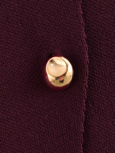 Detail der lila Stricktextur mit einem dekorativen goldenen Metallknopf als Akzent