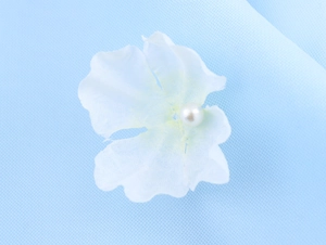 Detailed view of a white fabric flower with a pearl center on a blue mesh background
