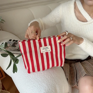 Detail of red and white striped canvas toiletry bag held by hands in a cozy setting