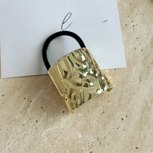 Macro detail of golden metal hair cuff with irregular water ripple texture and black elastic