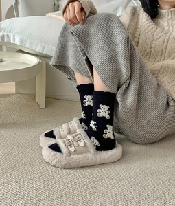 Close-up of cozy beige faux fur double-strap slippers with cute teddy bear socks