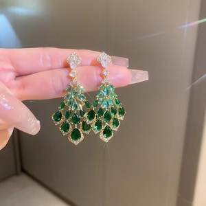 Detailed view of long gold tassel earrings with green teardrop stones and crystals