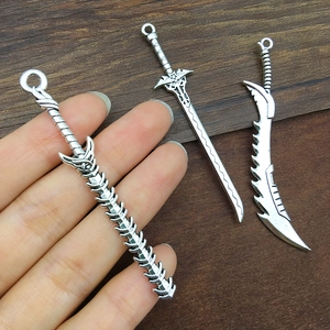 Three antique silver alloy sword pendants for DIY jewelry and keychains shown on a hand