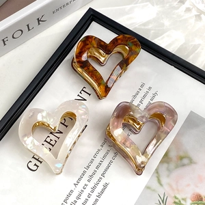 Three heart-shaped acetate claw clips in amber, pearly white, and transparent purple