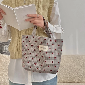 Détail du sac lunch en toile à carreaux avec nœud rouge tenu par un mannequin en vue