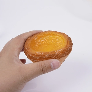 Hand holding a realistic 7.5cm Portuguese egg tart squishy toy with caramel texture