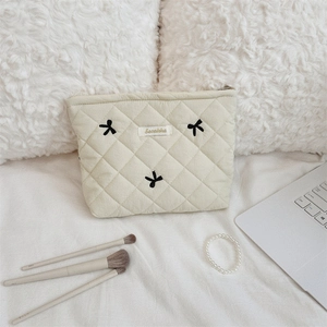 Detail of beige quilted makeup bag with black bow embroidery and gold logo on white sheets