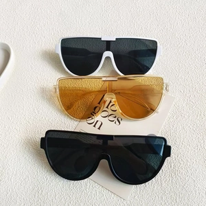 Flat lay of oversized flat top sunglasses in white, amber, and black on a textured surface