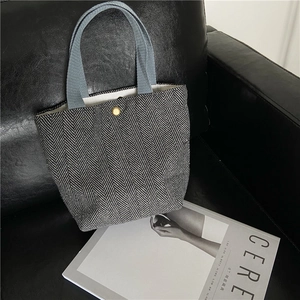 Detail view of herringbone canvas tote bag showing the snap button closure and blue handle