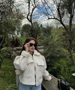 Close-up of white fuzzy sherpa jacket featuring lapel collar and metal zipper detail