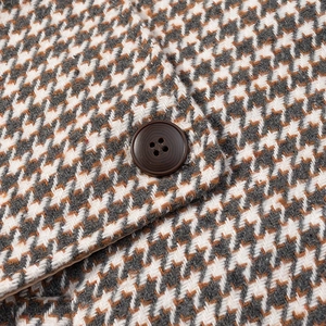 Detailed close-up of brown button on houndstooth texture wool coat in white and grey