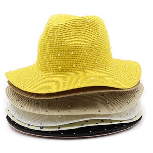 Close-up of colorful rhinestones on various straw sun hats in yellow, beige, and black