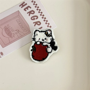 Close-up of white plush cat embroidery patch holding a red apple with fine details