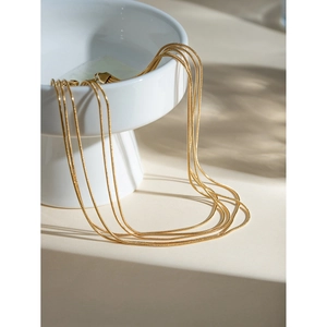 Close-up of elegant triple-layered 18k gold plated snake chain necklace on white ceramic