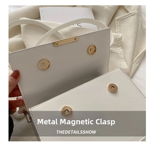 Close-up of white leather handbag with dual gold magnetic closures and fine stitching