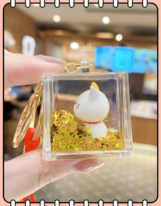 Macro shot of liquid glitter lucky cat keychain in acrylic cube with gold sequins