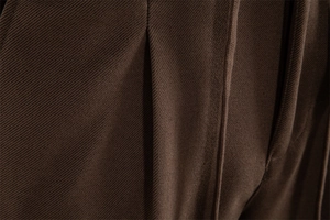 Detailed close-up of dark brown twill fabric texture and fine stitching on men's trousers