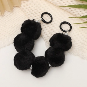 Detail of soft black plush pom-pom keychain with metal rings on textured fabric background