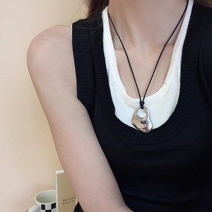 Close-up of a silver hollow heart pendant on a black cord necklace worn by a model