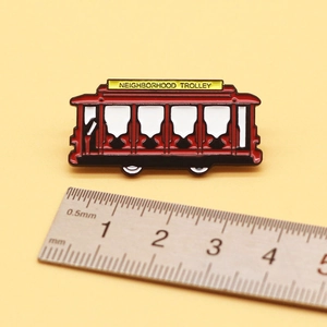 Close-up of red Neighborhood Trolley enamel pin showing 4.5cm width measurement