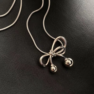 Detailed macro shot of silver bow pendant with spherical metal beads on a sleek snake chain
